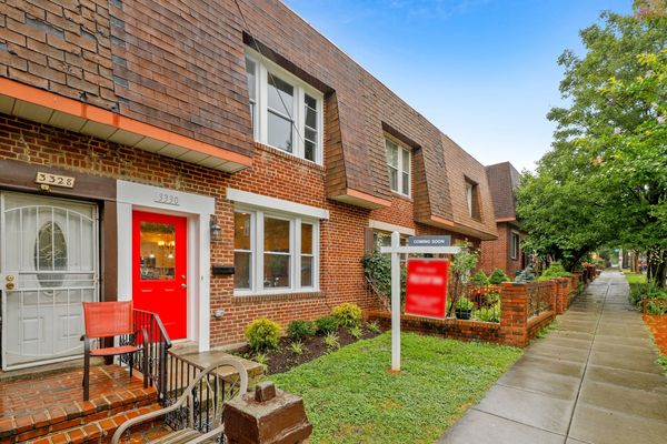 Brick townhouse with a red door and a 'Coming Soon' real estate sign on a green lawn.