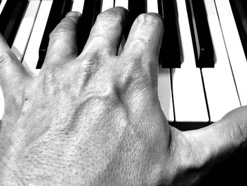Close-up of a hand playing piano keys in black and white.