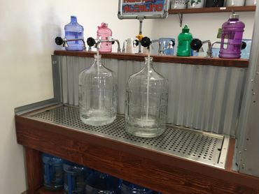 Two 5 gallon glass bottles being filled with alkaline water