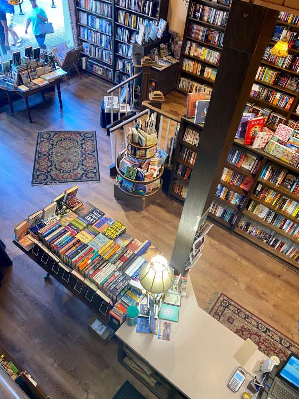 Cozy bookstore interior with wooden shelves, tables, and a decorative rug.