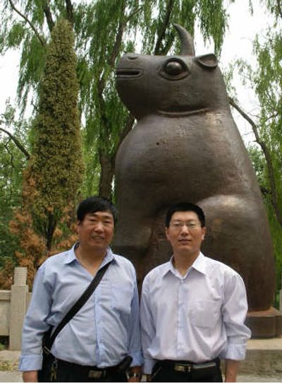 Two men standing in front of a large bull statue outdoors.