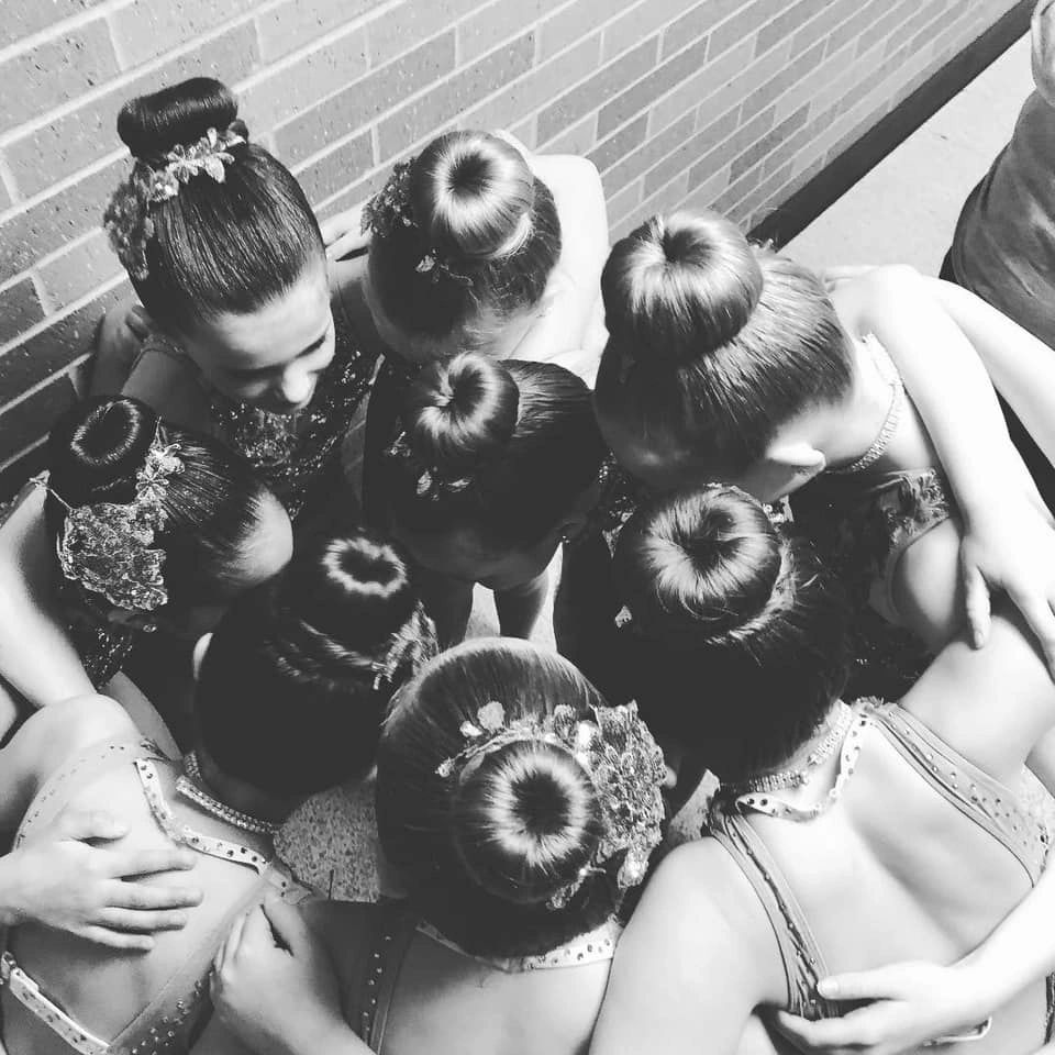 A group of dancers huddled together with elegant buns and costumes.