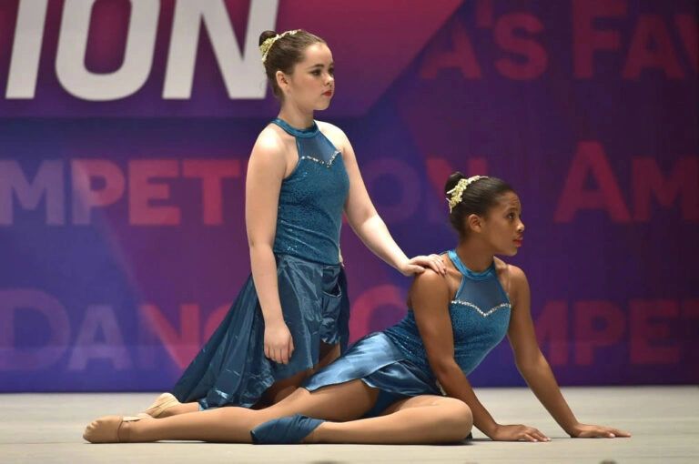 Two young dancers in blue costumes performing on stage at a competition.