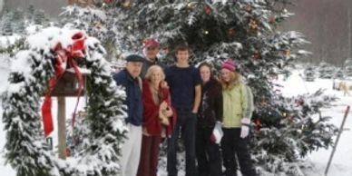 A photo showing a family standing in a snow covered landscape in front of a tall snow covered tree