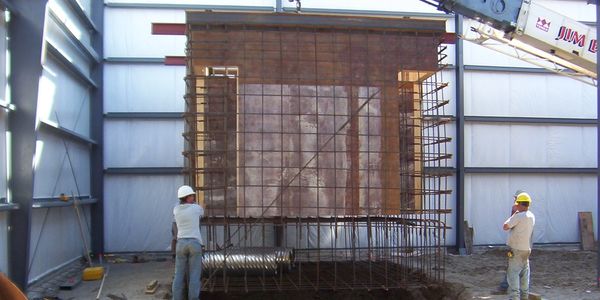 Crane lifting prefabricated form system into a trench for pouring a concrete press pit