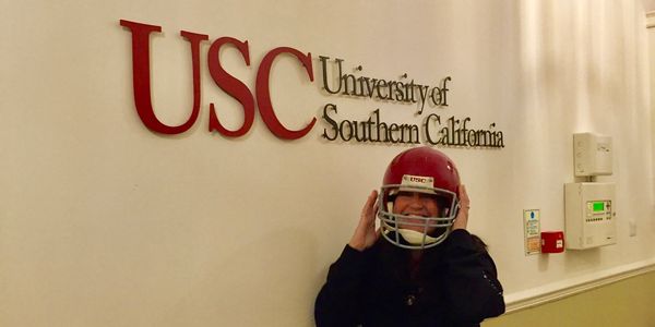 Woman wearing USC football helmet in front of an indoor sign of University Of Southern California