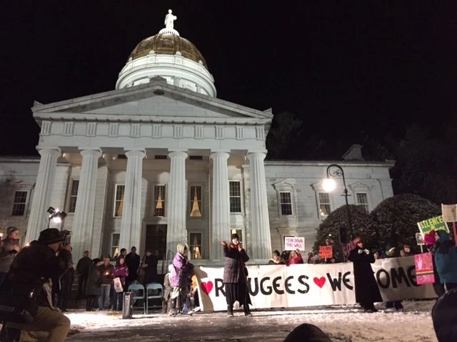 Crowd rallies in front of VT statehouse with a sign reading "Refugees Welcome" as a speaker shares.