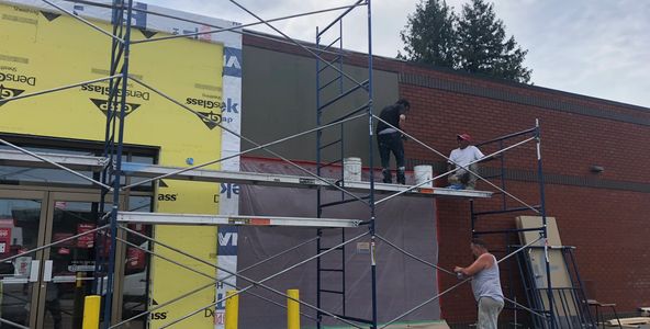 Workers on scaffolding working on stucco,  siding, and brick finished wall.