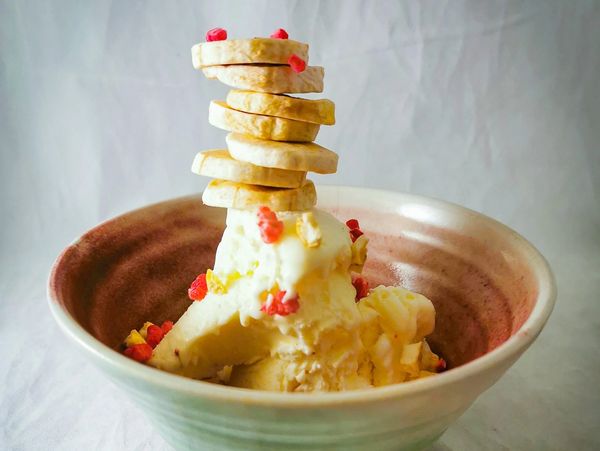 A bowl of vanilla icecream with a stack of freeze dried banana slices and raspberry crumble sprinkle