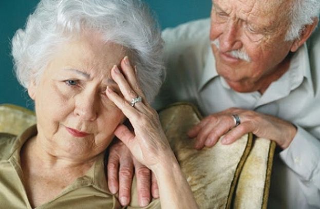 Elderly woman appears distressed, elderly man consoles her.