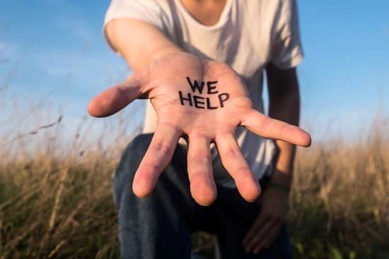 Person showing an open hand with 'WE HELP' written on the palm outdoors.
