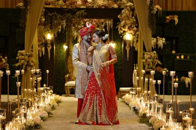 The Indian bride in red against the mandap in gold and Aisle laid with blush flowers and gold votive
