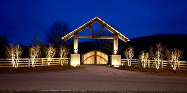 Custom wood entrance with rock columns, four plank fence, and landscape lighting