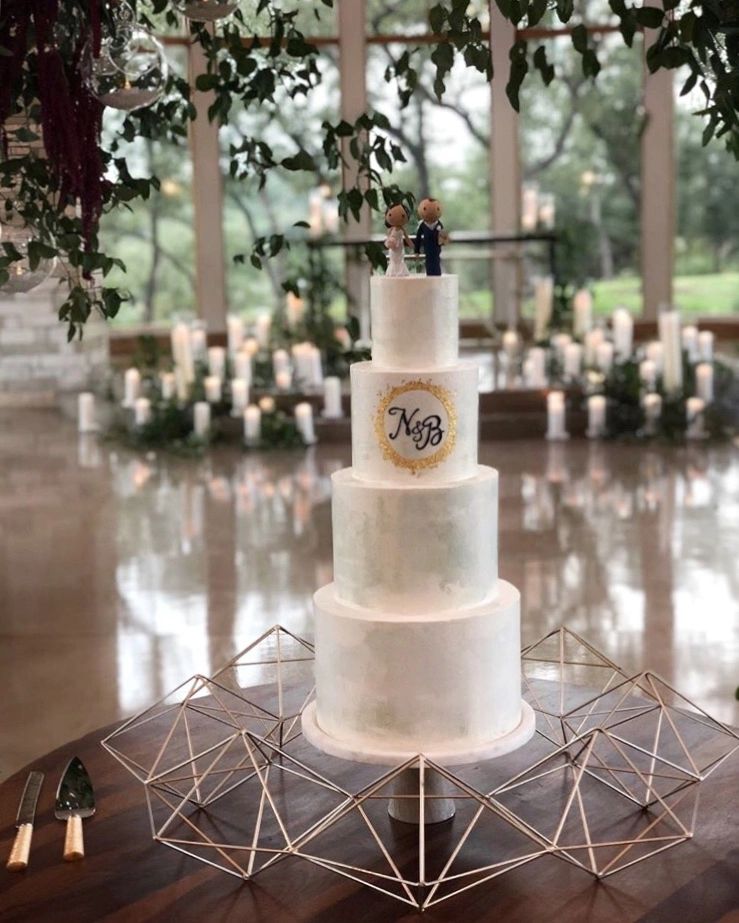 four tiered wedding cake with bride and groom toppers sits in front of ceremony site.