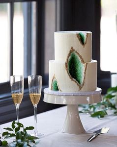 2 tiered white wedding cake with green geodes carved into front, next to 2 glasses of champagne.