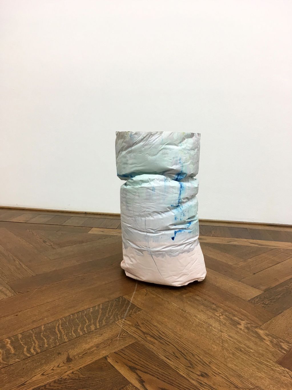 A crumpled, painted cylindrical object on a wooden floor.