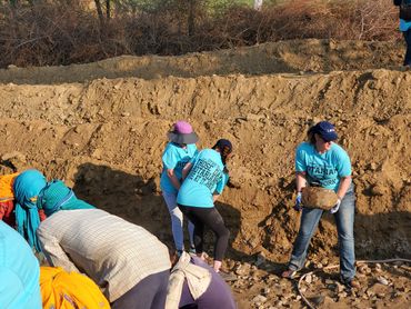 Volunteers in blue shirts working together on a rocky dirt slope outdoors.