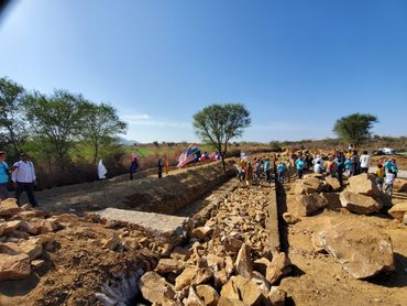 People exploring an ancient archaeological site with stone ruins and dirt pathways under a clear sky.
