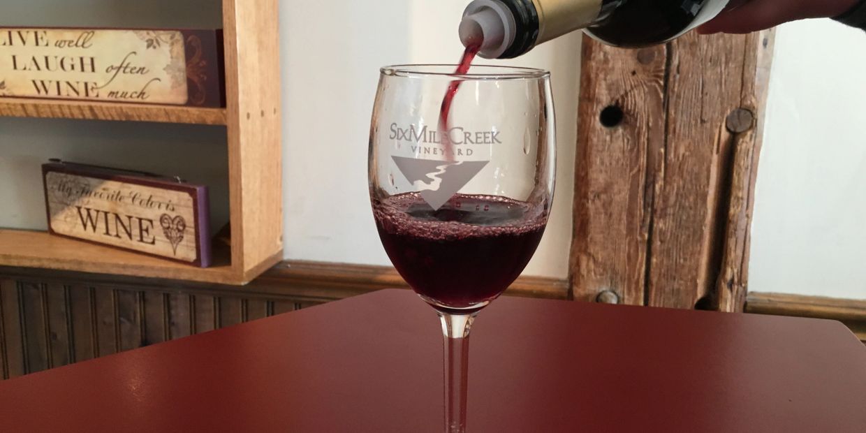 a red wine being poured into a six mile creek wine glass