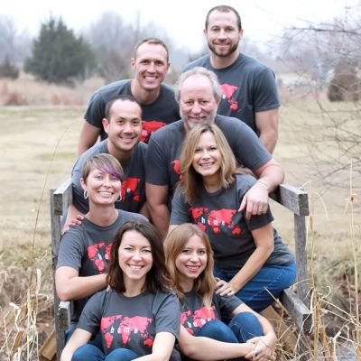 Group of eight people posing outdoors wearing matching t-shirts.