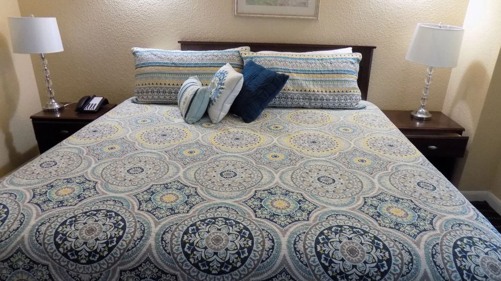 A neatly made bed with a patterned bedspread, two nightstands, and lamps in a guest room.
