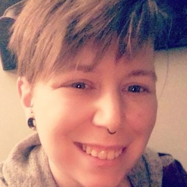 Close-up smiling person with short hair and septum piercing.