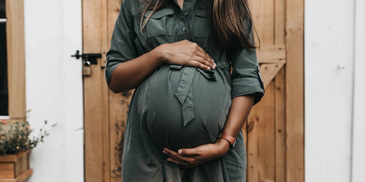 Pregnant woman gently holding her baby bump in front of a wooden door.