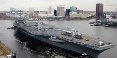 Aircraft carrier in water in with Norfolk VA skyline as background. Norfolk Movers support military.