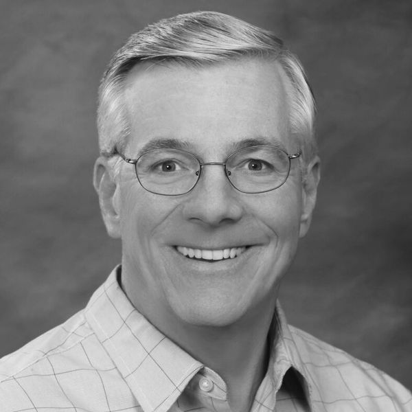Smiling middle-aged man wearing glasses and a checked shirt.
