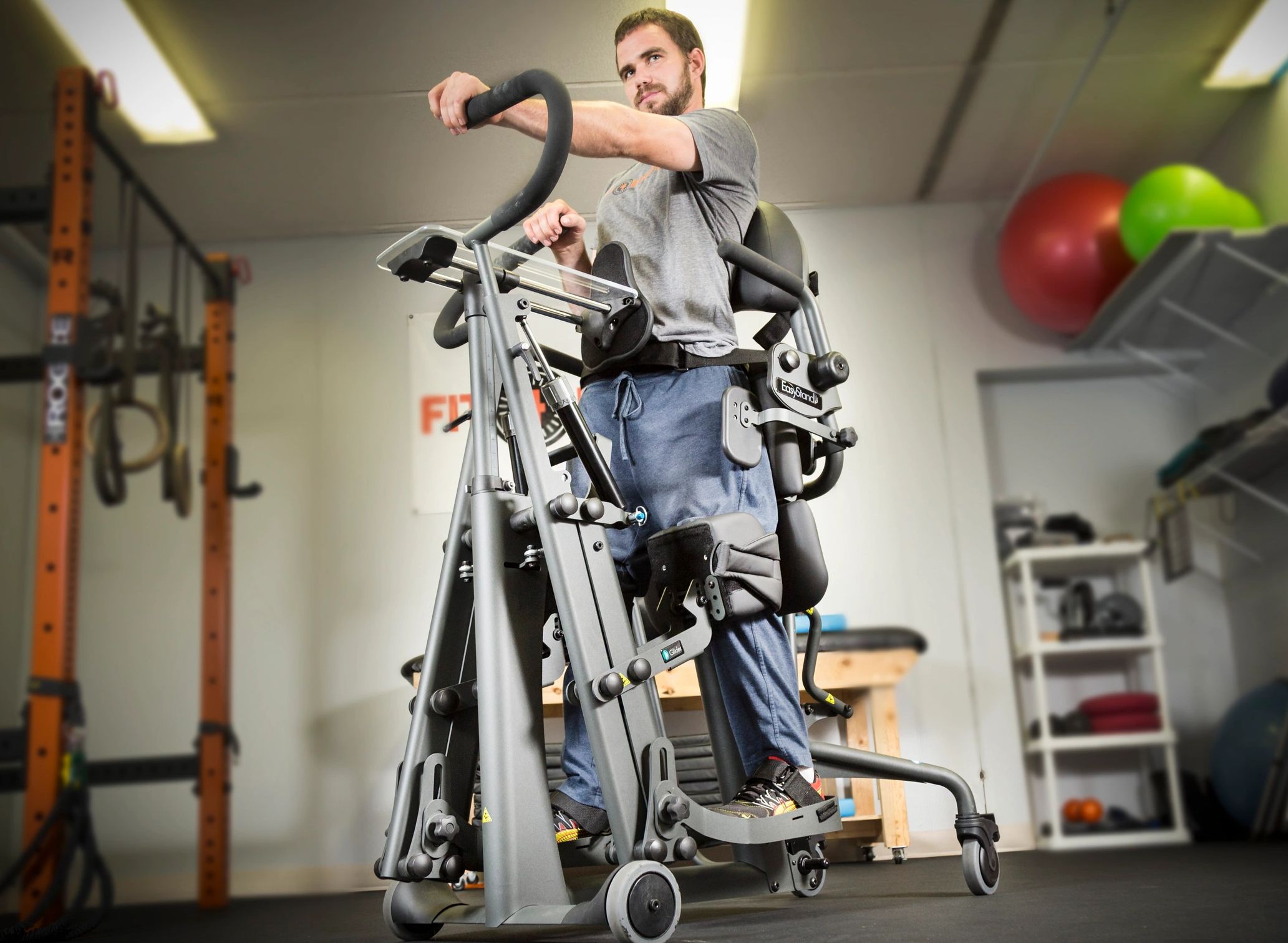 A man standing in an EasyStand Glider dynamic standing frame.  His left arm is  extended forward.