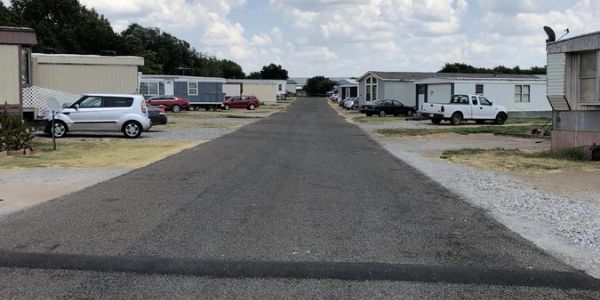 A quiet street in a mobile home park with parked cars on both sides.