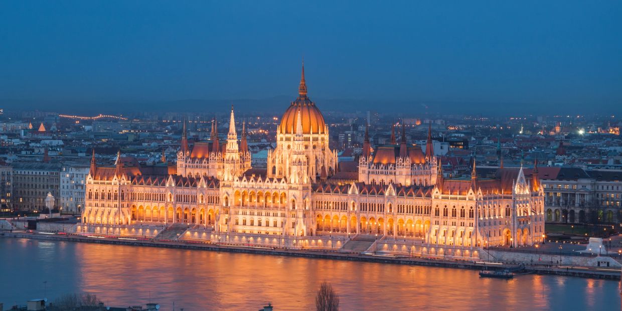 Illuminated Hungarian Parliament building reflecting on the Danube at dusk.