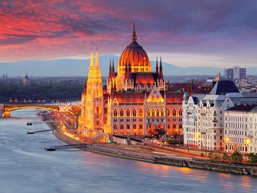 Illuminated Hungarian Parliament building at sunset by the Danube River.