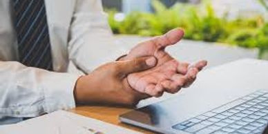 man holding wrist at laptop