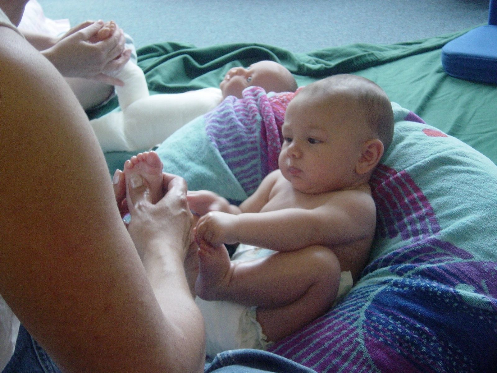 Adult holding a baby's foot while baby sits on a colorful cushion.