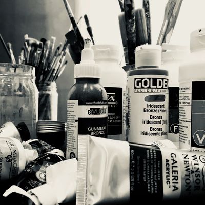 A close-up of various paint tubes and brushes in black and white.