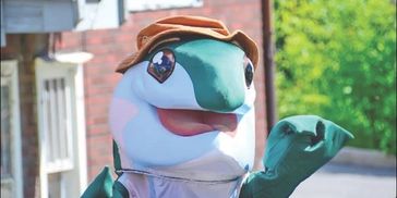Person in a gecko mascot costume waving outdoors.