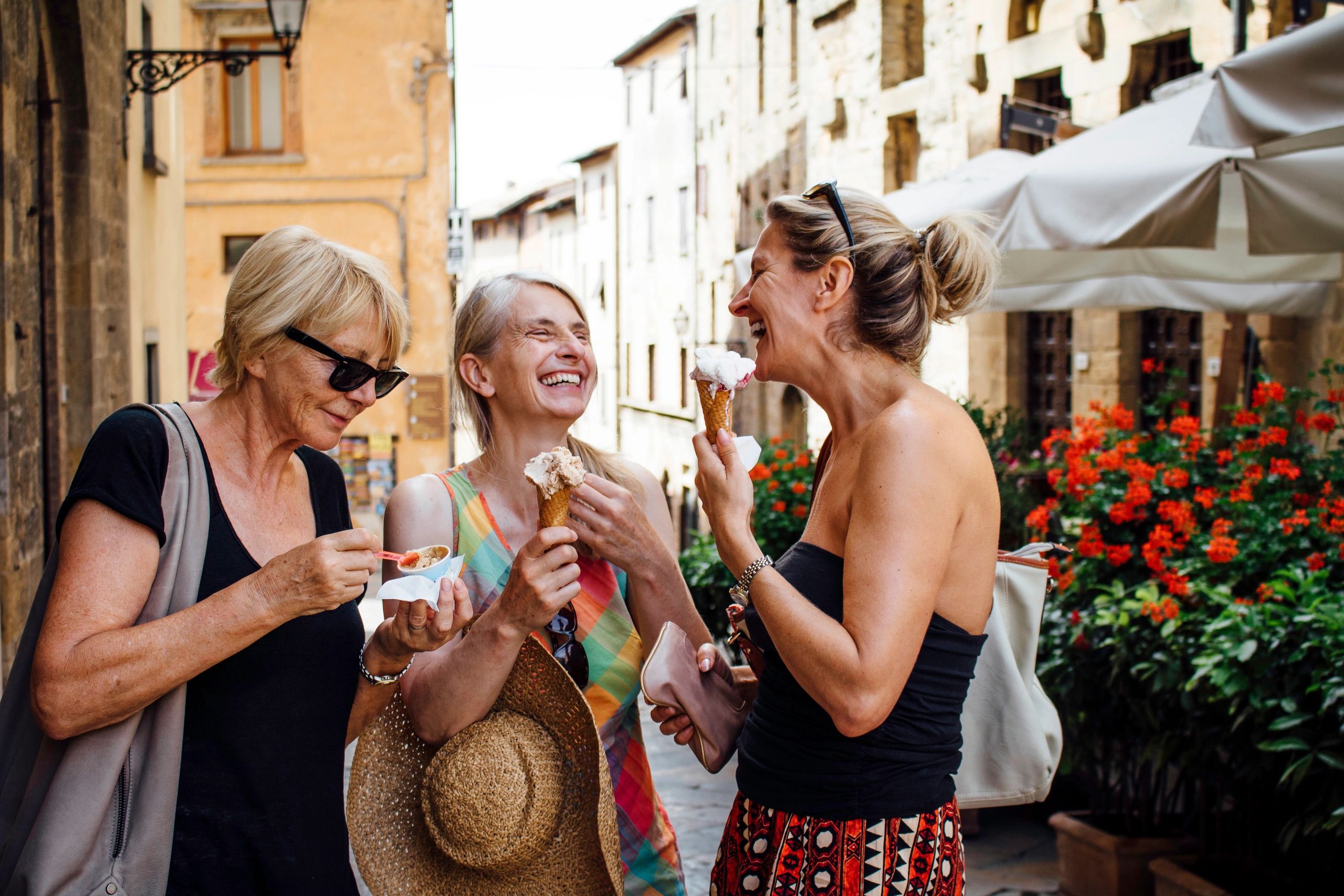 Three women enjoying ice cream and laughing outdoors.