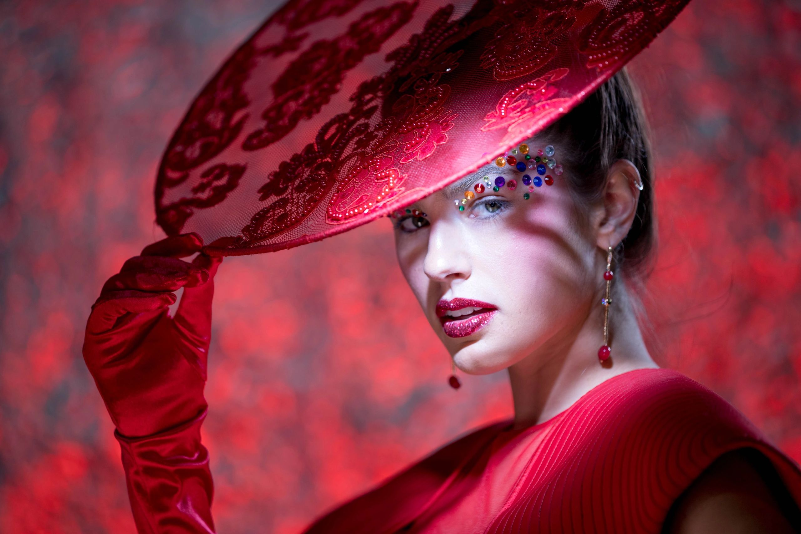Woman in red hat and gloves with decorative face jewels.
