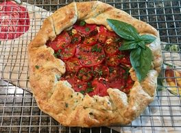 Tomato galette topped with fresh basil and parsley on a cooling rack.