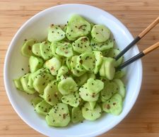 Marinated cucumbers in a white bowl with chopsticks.
