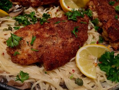 Chicken piccata served over angle hair pasta in a lemon cream sauce with mushrooms and parsley.