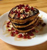 Pancakes topped with pomegranate seeds and chopped walnuts that are drizzled in syrup.