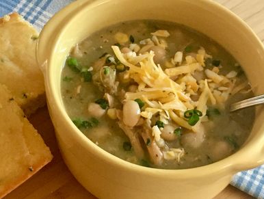 White bean chicken chili served in a yellow bowl, garnished with cheese, and cornbread on side.