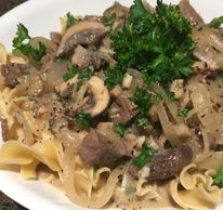 Beef Stroganoff served over egg noodles and garnished with fresh parsley and black pepper.