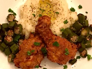 Fried chicken drumsticks served with okra and mashed potatoes with a butter pool.