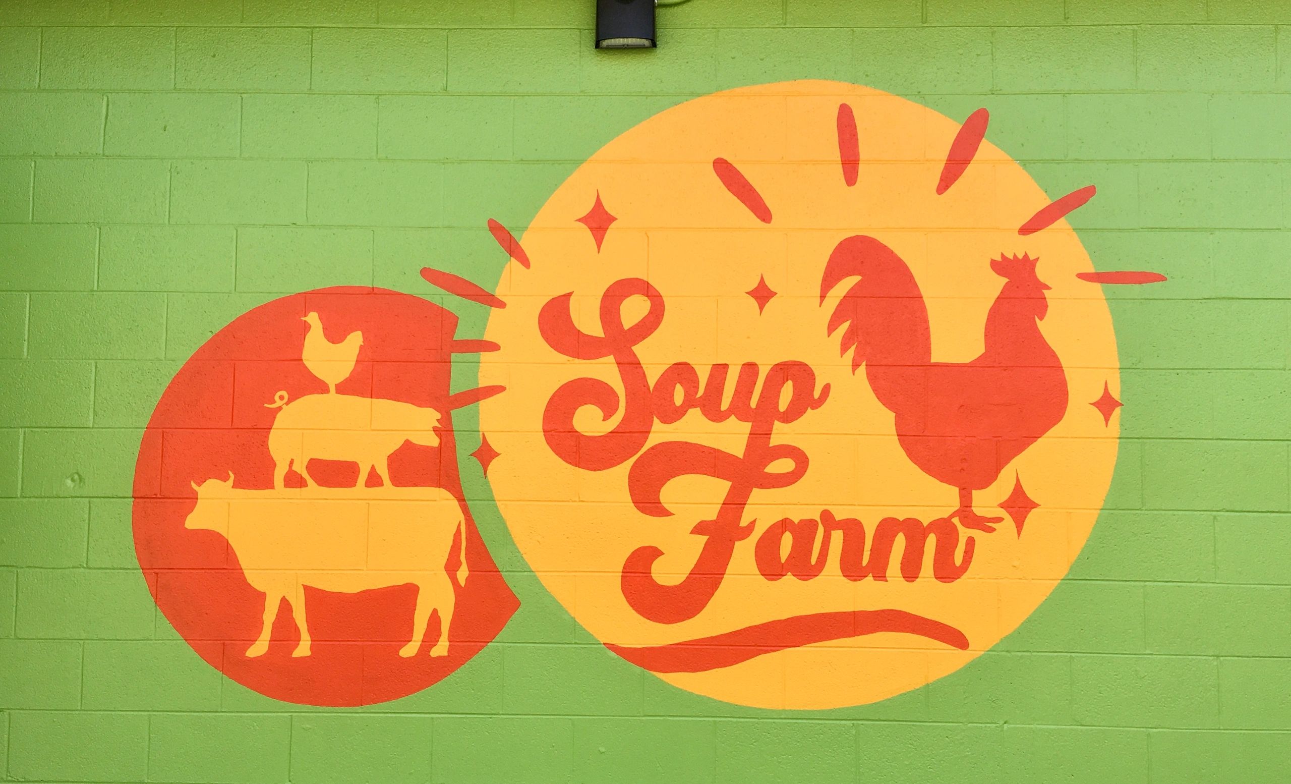 Green brick background wall with yellow and orange Soup Farm logo painted by Bridey O'Brien