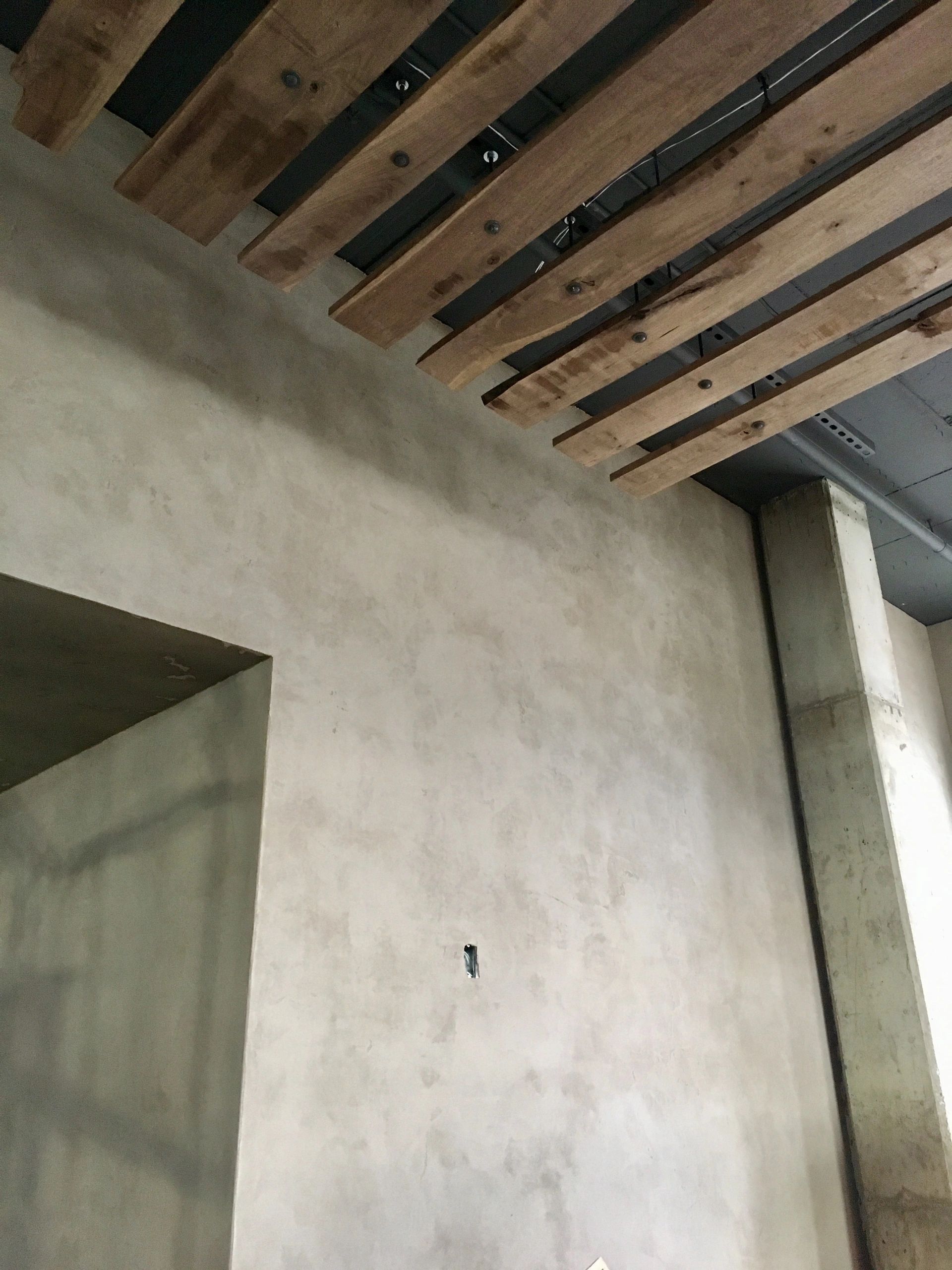 Low-angle photo of American Clay Forte plaster walls and doorway under a wood beam ceiling 
