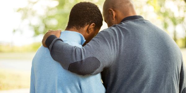 Older man with arm around younger man in support.