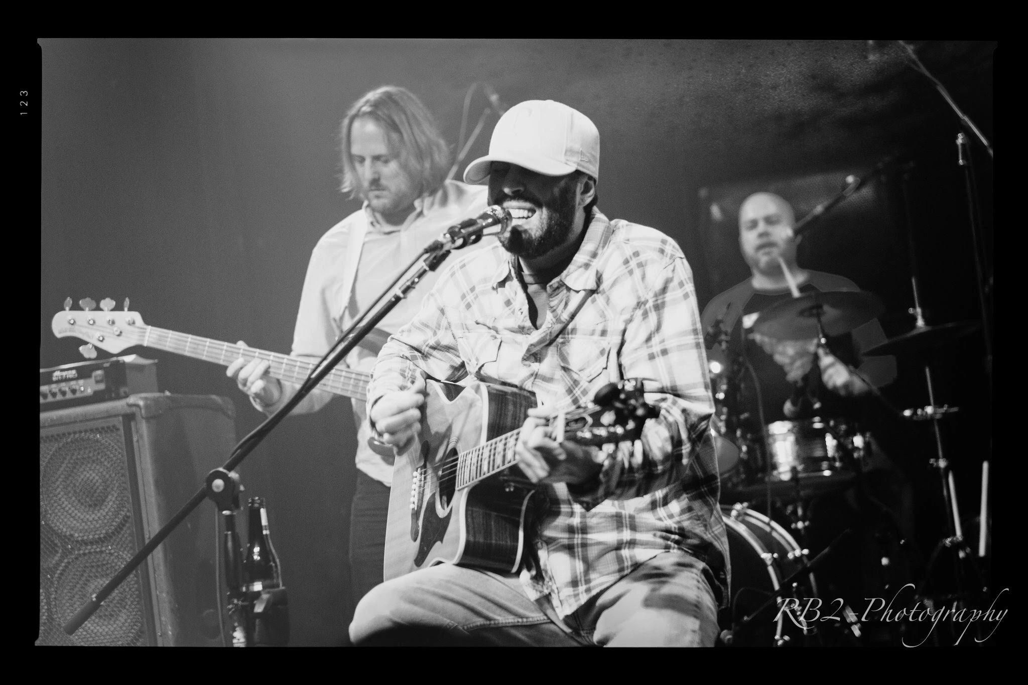 Grades Of Absolute Truth
Performing with a microphone and guitar with a bass player and a drummer